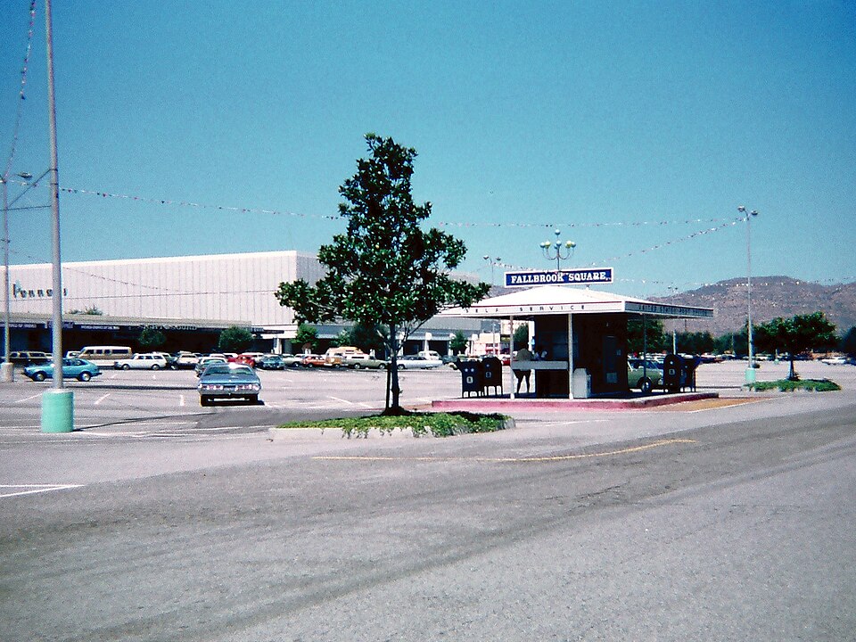 Exterior view of a former shopping center with parking lot and signage.