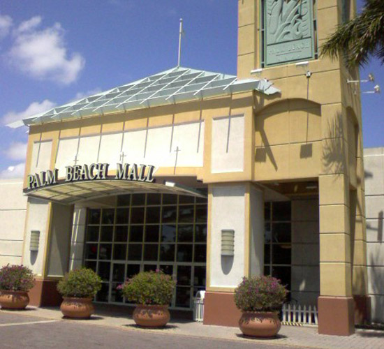 Exterior view of a shopping mall entrance with large glass windows and potted plants.